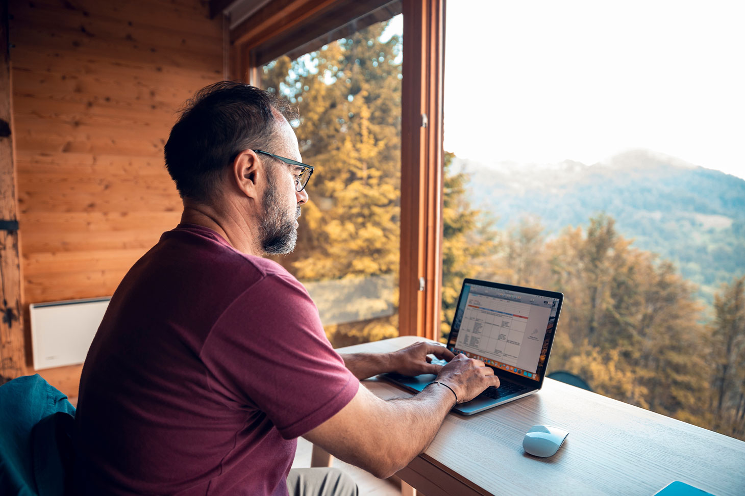 Un homme travaille sur son ordinateur portable sur un bureau situé face à un panorama de montagne